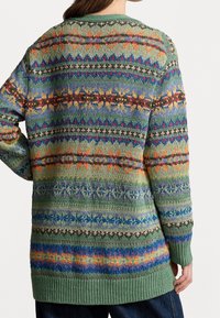 Stickad tröja i grönt med flerfärgade geometriska mönster. Har långa ärmar, ribbade muddar och en avslappnad passform. Strukturdetalj i garnet.