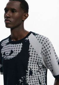 Strik kortærmet sweater med et navy og gråt rutenet mønster samt abstrakte designelementer. Glat tekstur og rund halsudskæring.