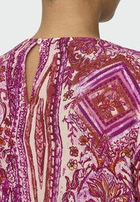 Blouse à motifs floraux colorés avec des teintes roses et violettes, présentant une fermeture arrière en forme de trou de serrure et un tissu doux et texturé.
