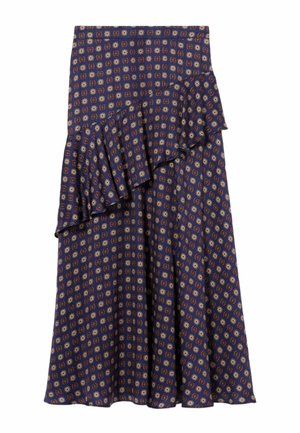 Donna con capelli lisci e scuri indossa un abito blu navy a maniche lunghe con motivi geometrici, balza asimmetrica e stivali neri al ginocchio, in piedi.