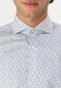 Witte blouse met een blauw bloemmotief, met een button-down kraag en standaard knoopsluiting. De stof ziet er glad uit met een lichtgewicht textuur.