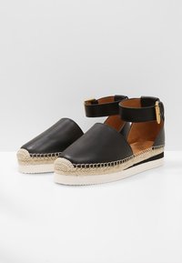 Espadrilles de cuero negro con tira al tobillo, plataforma envuelta en yute, textura suave y detalles de costura en contraste.