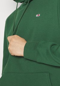 Sudadera verde hecha de un tejido de mezcla de algodón, con un bolsillo delantero, puños acanalados y un pequeño logotipo en el pecho.