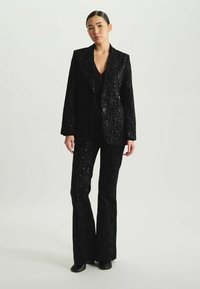 Ensemble de blazer noir à sequins et pantalon évasé, mettant en avant un motif floral texturé, une coupe ajustée, et une fermeture à un bouton sur la veste.