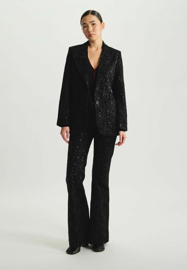 Ensemble de blazer noir à sequins et pantalon évasé, mettant en avant un motif floral texturé, une coupe ajustée, et une fermeture à un bouton sur la veste.