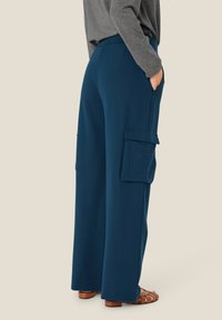 Brede cargobroek in donker teal, gemaakt van een soepele stof. Bevat twee zijzakken en een comfortabele elastische tailleband.