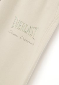 Beige Baumwollstoff mit "Everlast" und "Dance Division" aus silbernen und schillernden Strasssteinen. Glatte Textur, minimalistisches Design.