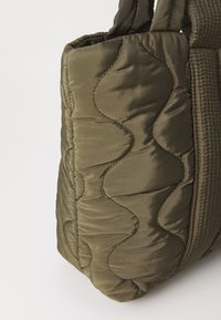 Bolsa de tote de nylon verde acolchada con patrón de olas; cuenta con lados acolchados y asas gruesas y texturizadas para mayor comodidad.