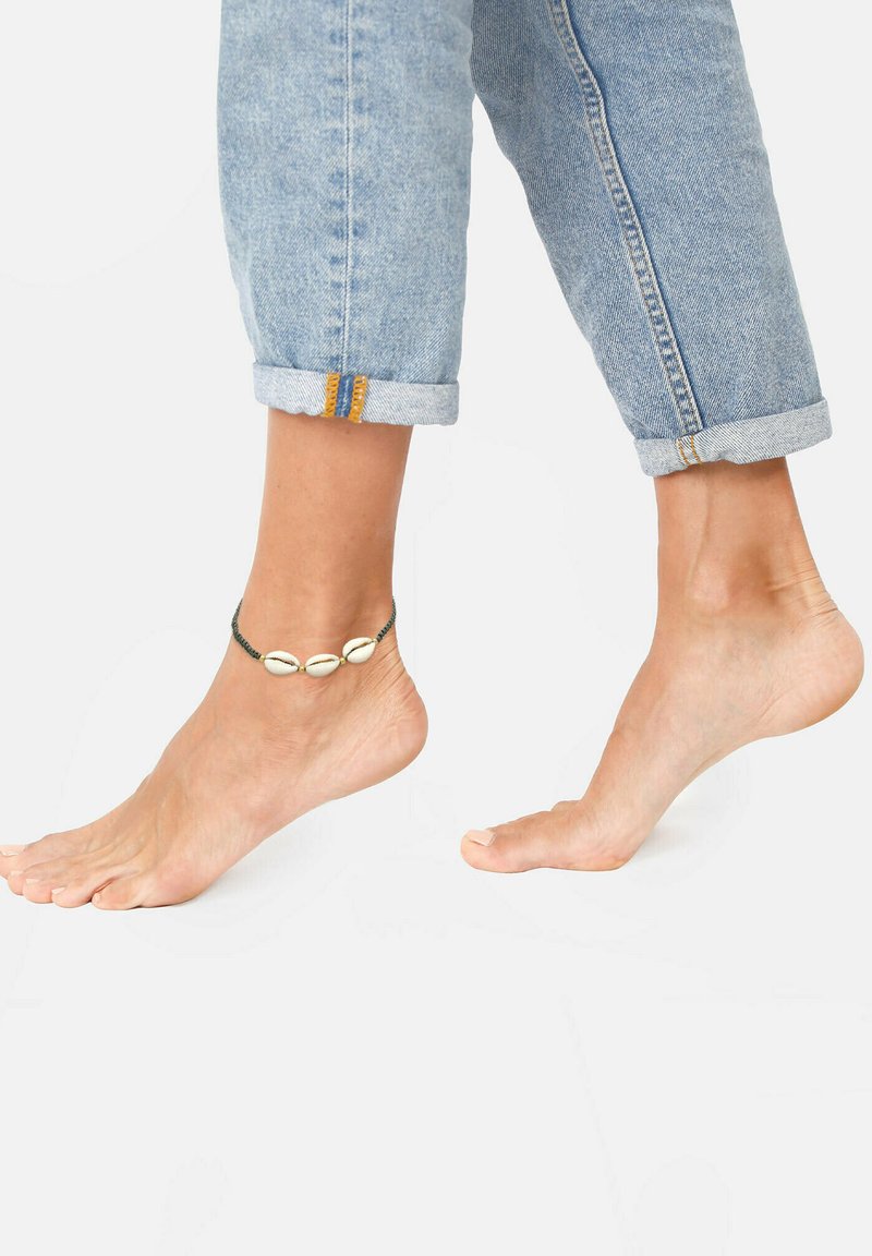 Anklet sa tri bijele školjke na tamnoj žici, nosi se na otkrivenoj članku, uparen s podvrnutim svijetloplavim trapericama.