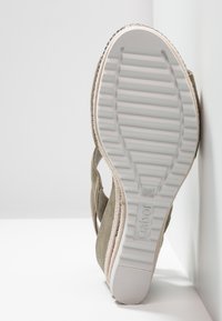 Grå mockaskor med en texturerad sida och en vit gummisula med räfflor. Sulan har präglingar med varumärkeslogotyp nära hälen.