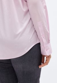 Ροζ ανοιχτόχρωμο πουκάμισο μακρυμάνικο με ομαλή υφή, καμπυλωτό τελείωμα, μανσέτες με κουμπιά και εφαρμοστή σιλουέτα, συνδυασμένο με σκούρο γκρι τζιν.