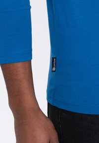 Blauwe, langarm t-shirt van katoen, met een hem label met een logo. Soepele textuur met een aansluitend ontwerp, zichtbare stikseldetails.