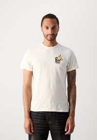 Lysecrèmet T-shirt lavet af blød bomuld. Har et farverigt grafisk design på brystet, med korte ærmer og en klassisk rund hals.