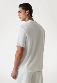 Weißes T-Shirt mit kurzen Ärmeln, Rundhalsausschnitt und glatter Textur, im entspannten Schnitt und mit schlichter Gestaltung.