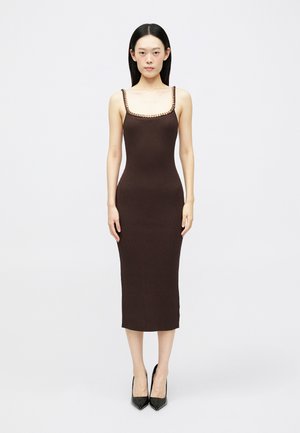 Robe midi marron à côtes avec des fines bretelles et une bordure décorative le long du décolleté, accompagnée de chaussures à talons pointus noires.