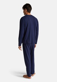 Conjunto de pijama de manga larga de color azul marino hecho de una tela suave; presenta un corte relajado con pantalones a juego y sin patrones ni acentos visibles.