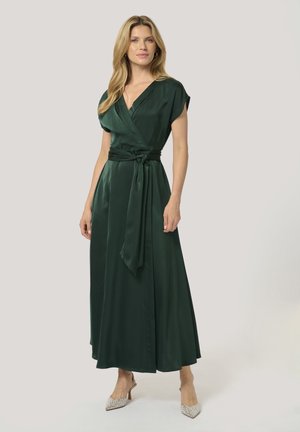 Green satin wrap dress with short sleeves and a tied waist. Features a deep V-neck and flows to ankle length, paired with embellished heels.
