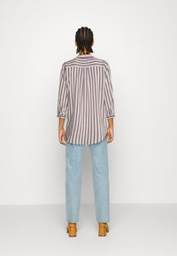 Camicia a maniche lunghe con righe verticali bordeaux e bianche, tessuto leggero, taglio dritto, abbinata a jeans azzurri chiari e tacchi a blocco color sabbia.