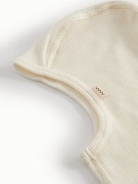 Cream-colored ribbed cotton baby hat with curved edges, featuring a small stitched label on the side and soft texture.