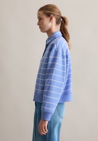 Lichtblauwe coltrui met witte horizontale strepen, voorzien van een relaxte pasvorm en geribbelde manchetten, gecombineerd met high-waisted jeans.