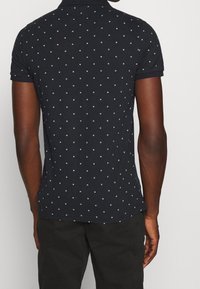 Mörknavy polo-shirts med en texturerad tyg, med ett mönster av små vita rutor. Korta ärmar och en klassisk kragsdesign.