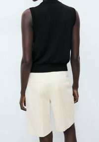 Top de punto negro sin mangas combinado con pantalones cortos color crema de corte a medida. Los pantalones cortos cuentan con dos bolsillos traseros y un diseño limpio y estructurado.