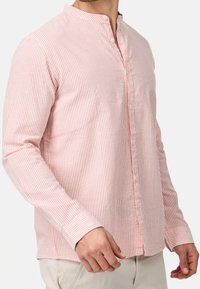 Camicia a righe rosa chiaro a maniche lunghe con collo alla coreana, chiusura con bottoni e tessuto strutturato. Presenta sottili righe bianche e maniche con polsini.