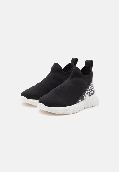 Ζευγάρι μαύρα sneakers χωρίς κορδόνια με λευκές σόλες και λεπτομέρεια κειμένου στο πλάι σε απλό λευκό φόντο.