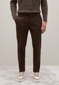 Bruine op maat gemaakte broek met een gladde stofafwerking. Gecombineerd met beige en witte sneakers met vetersluiting en gestructureerde accenten.