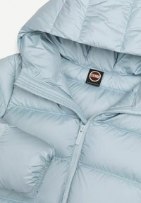 Veste matelassée bleu clair avec capuche, fermeture éclair à l'avant et poignets élastiques, montrant l'étiquette intérieure avec le nom de la marque Colmar.