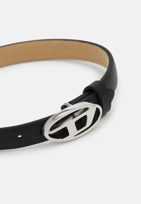 Black leather belt with a textured finish, featuring a silver oval buckle with cutout design. Underside is smooth, tan leather.