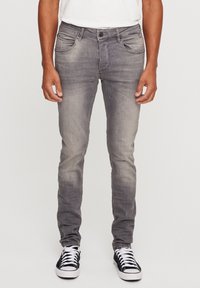 Vaqueros de mezclilla gris con un corte ajustado, acabado deslavado, cinco bolsillos y cierre de botón; combinados con zapatillas negras y blancas.