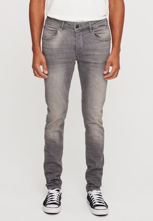Graue Jeans aus Denim mit schmalem Schnitt, verblasstem Finish, fünf Taschen und Knopfverschluss; kombiniert mit schwarz-weißen Sneakers.