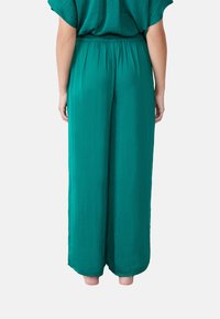 Brede groene broek gemaakt van lichtgewicht stof met een elastische tailleband, met een gladde textuur en zonder zichtbare patronen of accenten.