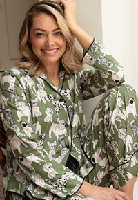 Piżama z długim rękawem wykonana z zielonego materiału z czarnymi lamówkami i wzorem przedstawiającym różne rasy psów w czarno-białych ilustracjach.