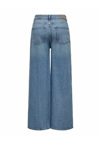 Jean en denim bleu clair à jambes larges avec des poches arrière et une étiquette en cuir avec logo sur la ceinture, vu de dos.