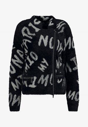 Sort plysjakke med grå abstrakte bogstaver og nittepynt, med asymmetrisk lynlås og lynlåslommer.