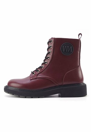 Bottine en cuir bordeaux avec lacets noirs, bout rond, semelle épaisse et patch logo circulaire sur le côté. Présente des œillets en métal argenté.