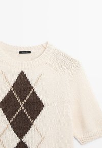 Crèmekleurige gebreide trui met bruin argyle ruitpatroon en korte mouwen, met een ronde halslijn en geribbelde kraag.