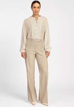 Crème blouse met knoopsluiting en een textuur aan de voorkant, met lange mouwen, gecombineerd met hooggetailleerde beige broek en bijpassende puntige schoenen.