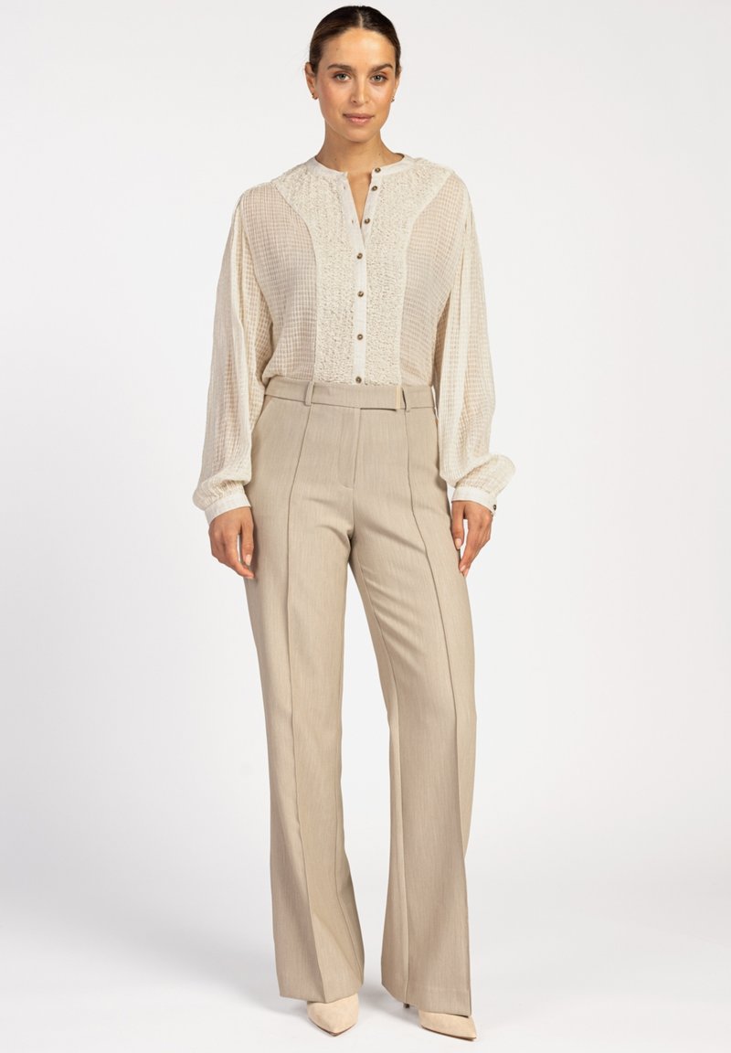 Crème blouse met knoopsluiting en een textuur aan de voorkant, met lange mouwen, gecombineerd met hooggetailleerde beige broek en bijpassende puntige schoenen.