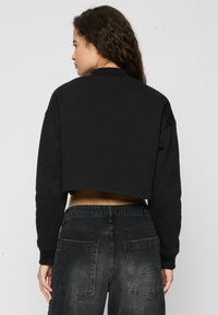 Svarte avkortede sweatshirt med rund hals og lange ermer; kombinert med mørkegrå, falmede jeans med baklommer og merkevare.