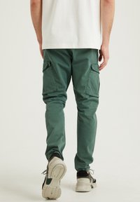 Gröna cargobyxor med flera sidofickor, en avsmalnande bendesign och en mjuk tygkänsla, kombinerat med neutralt färgade sneakers.