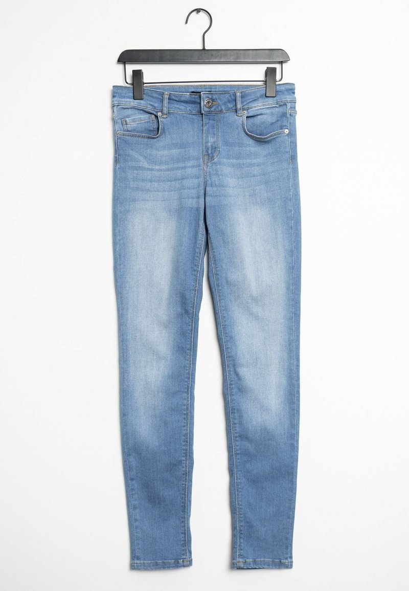 Jean skinny bleu clair avec poches avant, passants pour ceinture et fermeture par bouton, suspendu à un cintre noir sur un fond blanc.
