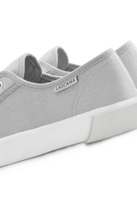 Graue Canvas-Slipper mit einer weißen Gummisohle, ausgestattet mit einem kleinen Markenetikett und strukturierten Stoffoberflächen.