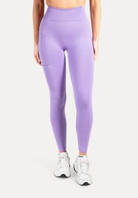 Lilla leggings med høj talje, glat tekstur og sidelomme. Båret med hvide sneakers for et komplet atletisk look.