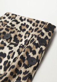 Tela de estampado de leopardo con tonos de marrón y negro. Presenta botones negros y un bolsillo con solapa en una superficie texturizada.