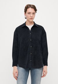 Mørkeblå, myk kordfløyelskjorte med spiss krage, knappestolpe foran og lange ermer, med en avslappet passform og subtil tekstur.