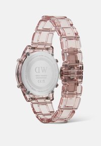 Montre translucide rose avec un bracelet en maillon et un dos en acier inoxydable. Présente un cadran circulaire et des détails clairs sur l'ensemble.