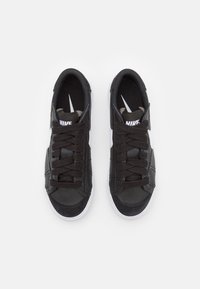 Black athletic sneakers with a smooth upper, featuring white accents, round laces, and a textured sole. Logo displayed on the tongue.